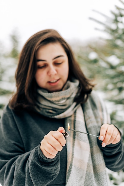 Erwachsene junge Frau mit Wunderkerzen auf Winterkiefernwald