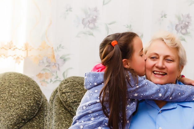 Erwachsene lächelnde Enkelkinder umarmen ältere Großmutter, die froh ist, sie vermisst zu sehen, Besuch liebender Verwandter genießen Kommunikation, Kuscheln als Symbol für Verbindung, Liebe und Unterstützungskonzept