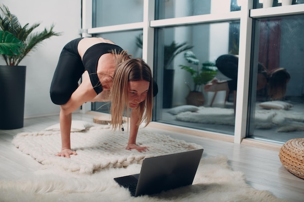 Erwachsene reife Frau, die Yoga zu Hause Wohnzimmer mit Online-Tutorials auf Laptop macht