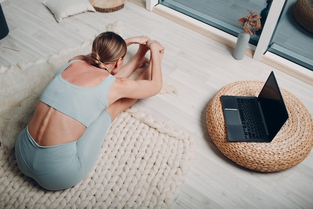 Erwachsene reife Frau, die Yoga zu Hause Wohnzimmer mit Online-Tutorials auf Laptop macht