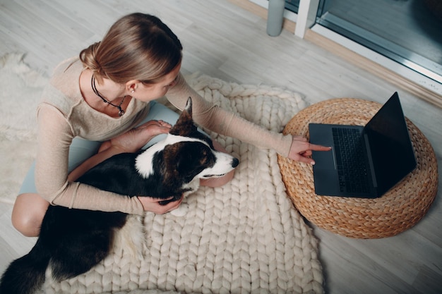 Erwachsene reife Frau macht Yoga zu Hause im Wohnzimmer mit Corgi Hund Haustier mit Online-Tutorials auf Laptop