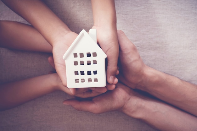 Erwachsene und Kinderhände, die weißes Haus, Familienheim und obdachloses Schutzkonzept halten