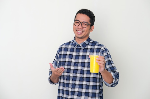 Erwachsener asiatischer Mann, der glücklich lächelt, während er eine Tasse frischen gelben Saftgetränks präsentiert