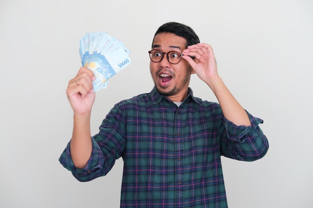 Erwachsener asiatischer Mann, der nach Geld sucht, das er mit erstauntem Ausdruck hält