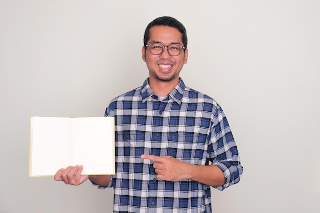 Erwachsener asiatischer Mann lächelt in die Kamera und zeigt auf leere Buchseiten, die er zeigt