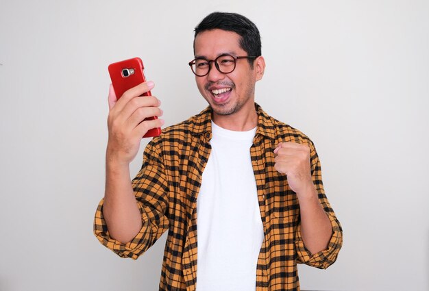 Erwachsener asiatischer Mann schaut mit aufgeregtem Gesichtsausdruck auf das Mobiltelefon, das er in der Hand hält