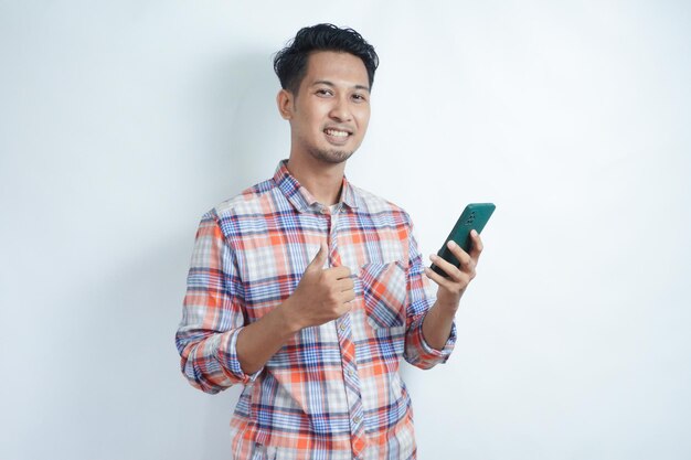 Erwachsener asiatischer Mann trägt ein Flanellhemd, lächelt und hebt den Daumen, während er ein Handy hält