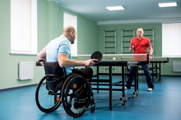 Erwachsener behinderter Mann im Rollstuhl spielen mit seinem Trainer beim Tischtennis