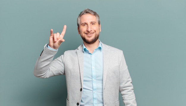 Foto erwachsener geschäftsmann, der sich glücklich, lustig, selbstbewusst, positiv und rebellisch fühlt und mit der hand rock- oder heavy-metal-zeichen macht