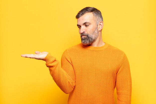 Erwachsener gutaussehender Mann, der sich glücklich fühlt und lässig lächelt und auf ein Objekt oder Konzept schaut, das auf der Hand auf der Seite gehalten wird