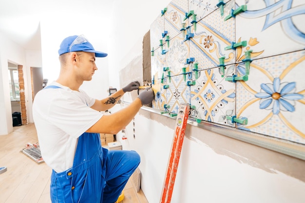 Erwachsener Handwerker in einer speziellen Uniform, der Fliesen mit Fliesennivellierungssystem an der Wand an der Küche in a legt