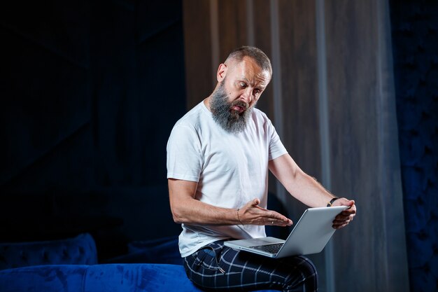 Erwachsener männlicher Geschäftsmann, Lehrer, Mentor, der an einem neuen Projekt arbeitet. Sitzt an einem großen Fenster auf dem Tisch. Er schaut auf den Bildschirm des Laptops.