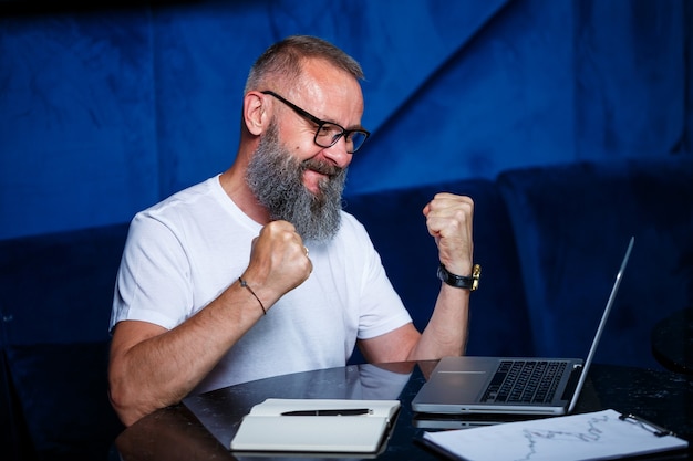 Erwachsener männlicher mentor, direktor, geschäftsmann in brille und anzug, der dokumente studiert, während er am tisch sitzt. konzept des arbeitstages