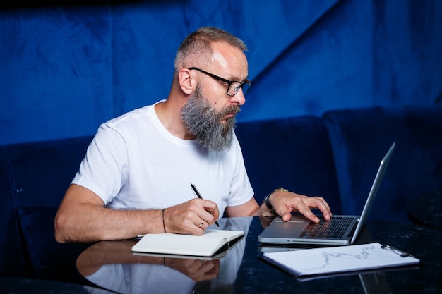 Erwachsener männlicher mentor, direktor, geschäftsmann in brille und anzug, der dokumente studiert, während er am tisch sitzt. konzept des arbeitstages