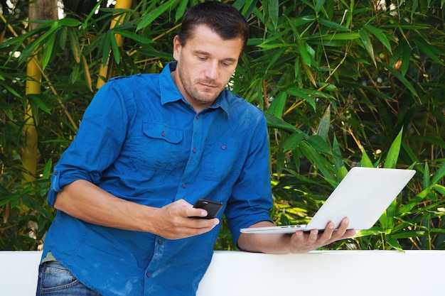 Foto erwachsener mann benutzt einen laptop gegen grüne blätter.