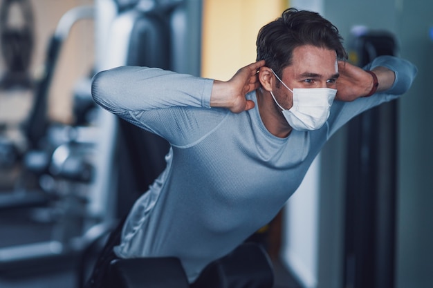 Erwachsener Mann, der aufgrund von Covid-19 in einem Fitnessstudio mit Maske trainiert