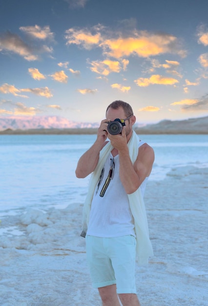 Erwachsener Mann Fotograf fotografiert mit Digitalkamera am Strand des Toten Meeres in Ein Bokek Israel Schöner muskulöser Mann mit Bild mit moderner dslr-Kamera am Strand von Seashore Travel