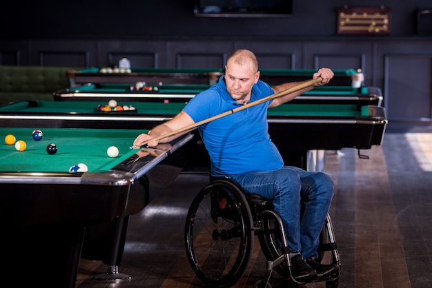 Erwachsener Mann mit Behinderung im Rollstuhl spielt Billard im Club