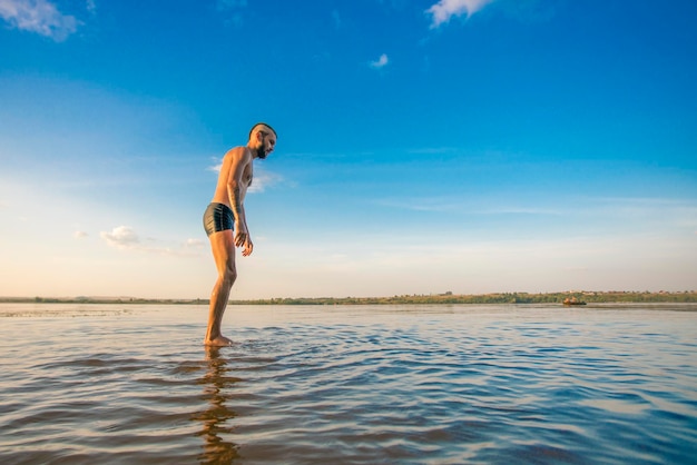 Erwachsener Mann mit Irokesenschnitt auf dem Kopf und schwarzen Shorts steht auf dem Wasser vor dem Hintergrund eines blauen Himmels mit Wolken