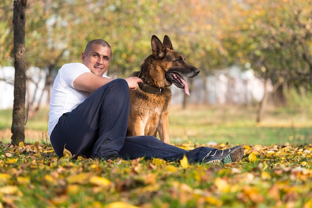 Erwachsener Mann sitzt mit seinem Deutschen Schäferhund im Freien