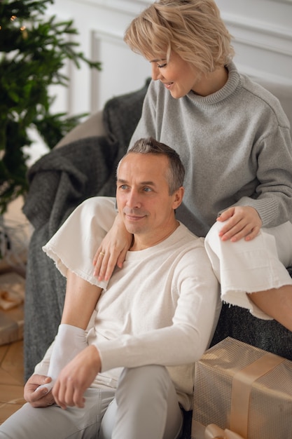 Erwachsener Mann und Frau sitzen auf dem Sofa neben dem Weihnachtsbaum und umarmen sich