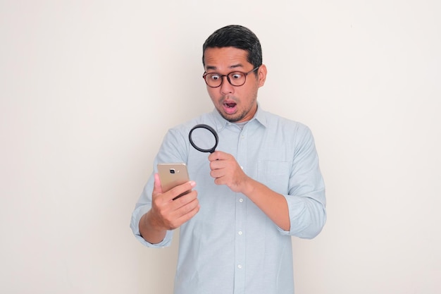 Foto erwachsener mann zeigt einen schockierten ausdruck, wenn er mit einer lupe auf ein handy schaut