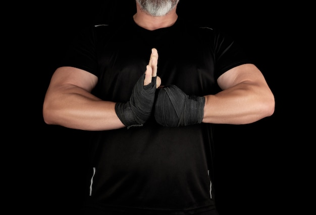 Erwachsener muskulöser Athlet in schwarzer Kleidung mit zurückgewickelten Händen mit einem schwarzen Verband schloss sich seinen Händen vor seiner Brust an