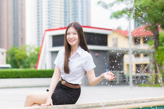 Erwachsener thailändischer Student in Universitätsstudentenuniform Asiatisches schönes Mädchen sitzt und schüttelt das Wasser