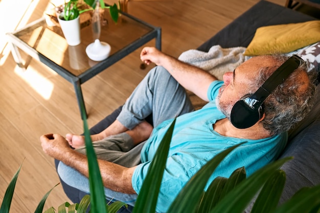 Foto erwachsener übergewichtiger mann mittleren alters mit drahtlosen kopfhörern, der sich zu hause mit geführter meditation entspannt