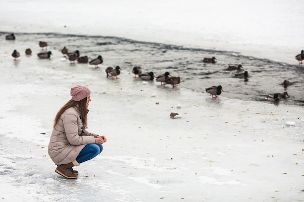 Erwachsenes Mädchen, das im Winter Enten auf dem zugefrorenen Fluss füttert