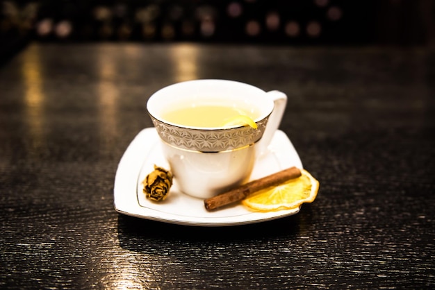 Erwärmender alkoholischer Cocktail in einer weißen Tasse auf dunklem Hintergrund die Bar mit einer Zimtstange und einer orangefarbenen Orange