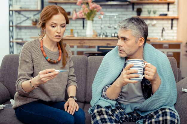 Erwärmendes Getränk. Netter kranker Mann, der mit einer Tasse Tee sitzt, während er mit seiner Frau spricht?