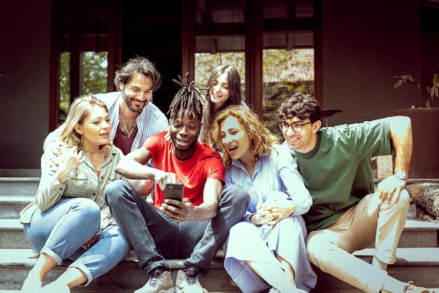 Erweitertes Familientreffen mit Adoptivkindern und Freunden, die lustige Momente beim Betrachten von Fotos auf Smart-Geräten haben, warmer und Vintage-Fotofilter