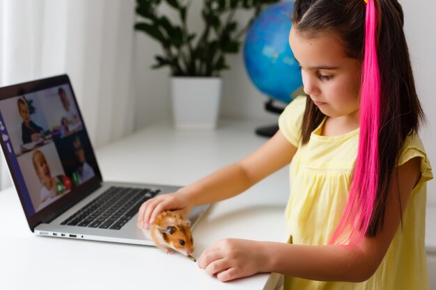 Erziehen Sie zu Hause. Kindermädchen machen Hausaufgaben mit Haustierhamster. Lustiger Ingwerhamster, der auf dem Tisch sitzt, in dem das Kind schreibt. Zurück zur Schule.