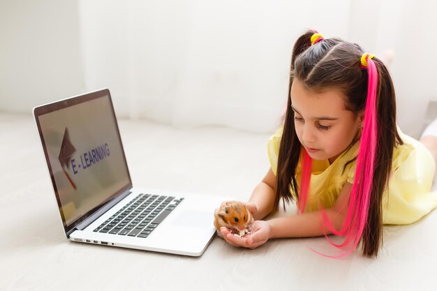 Erziehen Sie zu Hause. Kindermädchen machen Hausaufgaben mit Haustierhamster. Lustiger Ingwerhamster, der auf dem Tisch sitzt, in dem das Kind schreibt. Zurück zur Schule.