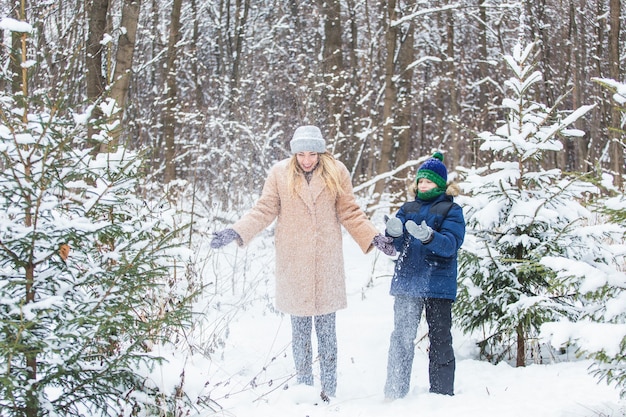 Erziehungs-, Spaß- und Saisonkonzept - Glückliche Mutter und Sohn, die Spaß haben und mit Schnee im Winterwald spielen.