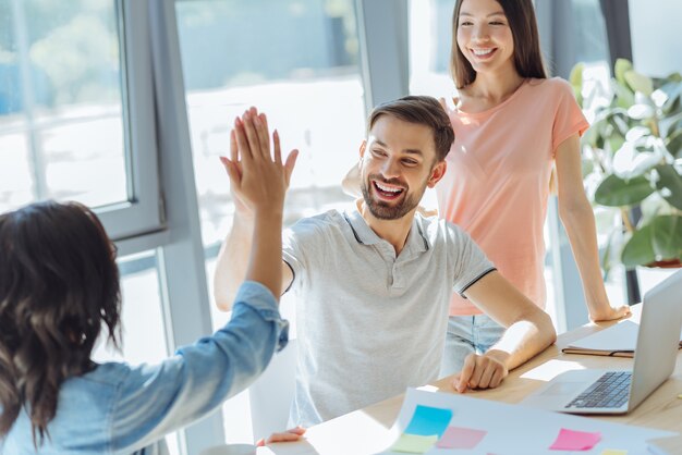 Esto es un acierto. Feliz alegre hombre positivo sonriendo y mirando a su colega mientras le da cinco