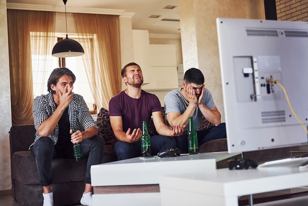 Es una derrota. Triste tres amigos viendo fútbol en la televisión en casa juntos.