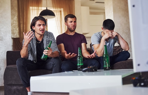 Es una derrota. Triste tres amigos viendo fútbol en la televisión en casa juntos.