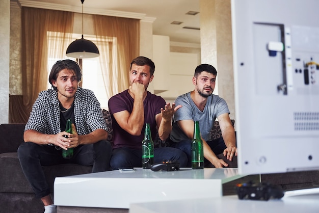 Es una derrota. Triste tres amigos viendo fútbol en la televisión en casa juntos.