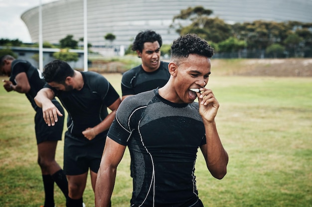 Es la foto recortada del medio tiempo de un apuesto joven jugador de rugby quitándose el protector bucal durante el medio tiempo en el campo