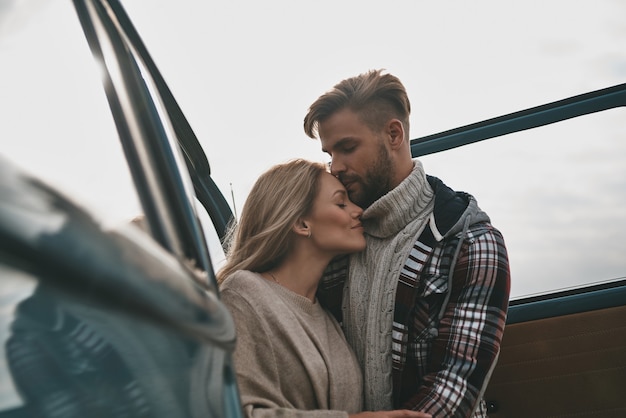 Es genial estar juntos. Hermosa joven pareja abrazándose y sonriendo mientras está de pie al aire libre cerca de la mini furgoneta de estilo retro