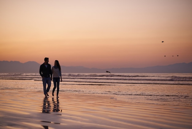 Es gibt nichts Schöneres als junge Liebe Silhouette eines jungen Paares, das einen romantischen Spaziergang am Strand genießt