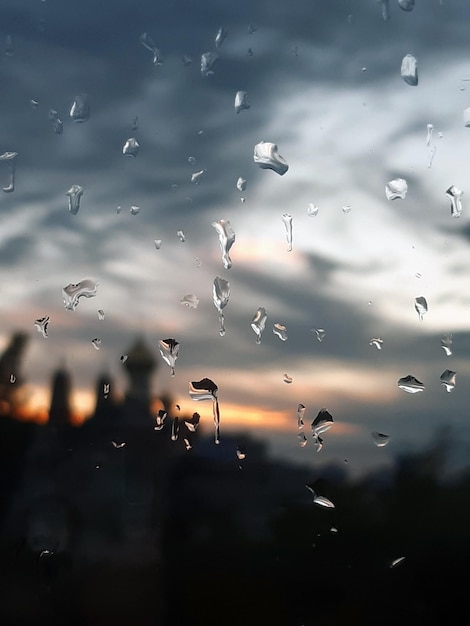 Es gibt viele Wassertropfen auf dem Glas Verschwommene Gebäude und Abendhimmel hinter dem Glas