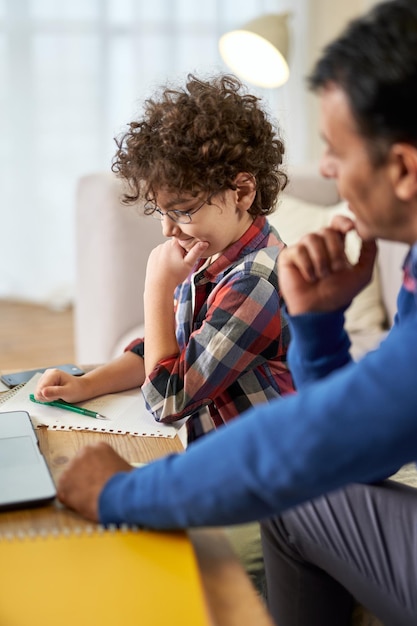 Es hora de aprender curioso niño de escuela latina haciendo la tarea junto con su padre escribiendo