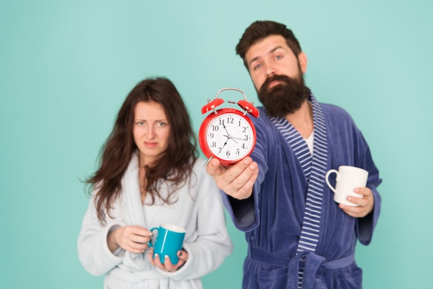 Es la hora del café. El hombre con barba y la mujer soñolienta disfrutan de té o café por la mañana. Chico en ropa de baño tiene té y café. Concepto de desayuno. Cada mañana comienza con un café. Pareja en albornoces con tazas.