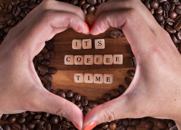 Es la hora del café con letras de un cubo de madera y una mujer haciendo un corazón con las manos