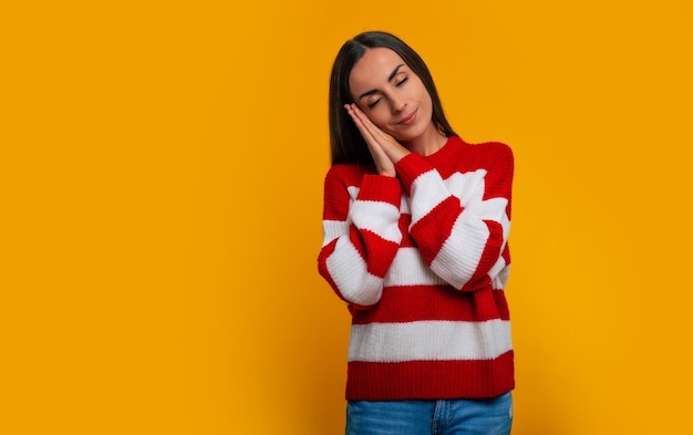 Es hora de dormir y relajarse. Retrato de una hermosa joven tranquila en un suéter de invierno aislado en el fondo amarillo mientras se prepara para dormir