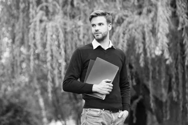 Es hora de estudiar maestro de escuela hombre sostener cuaderno chico guapo caminar con libros de trabajo en el parque estudiante de educación de la vida moderna obtener información del libro estudiante guapo sin afeitar que va a estudiar al aire libre