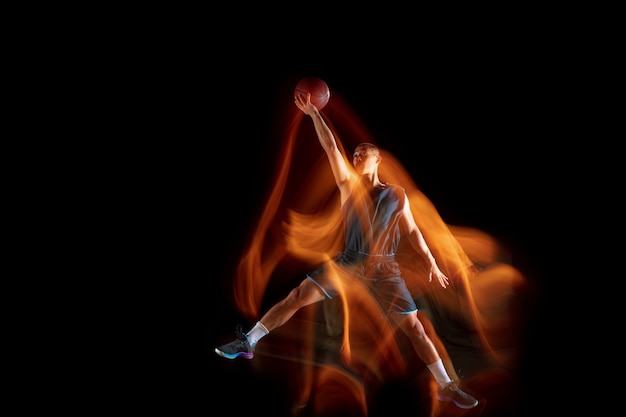 Es hora de ganar. Joven jugador de baloncesto del este asiático en acción y movimiento saltando en luz mixta sobre fondo oscuro de estudio. Concepto de deporte, movimiento, energía y estilo de vida dinámico y saludable.